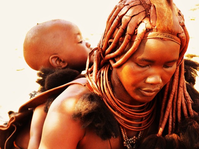 Himba woman with glowing skin carrying baby on back
